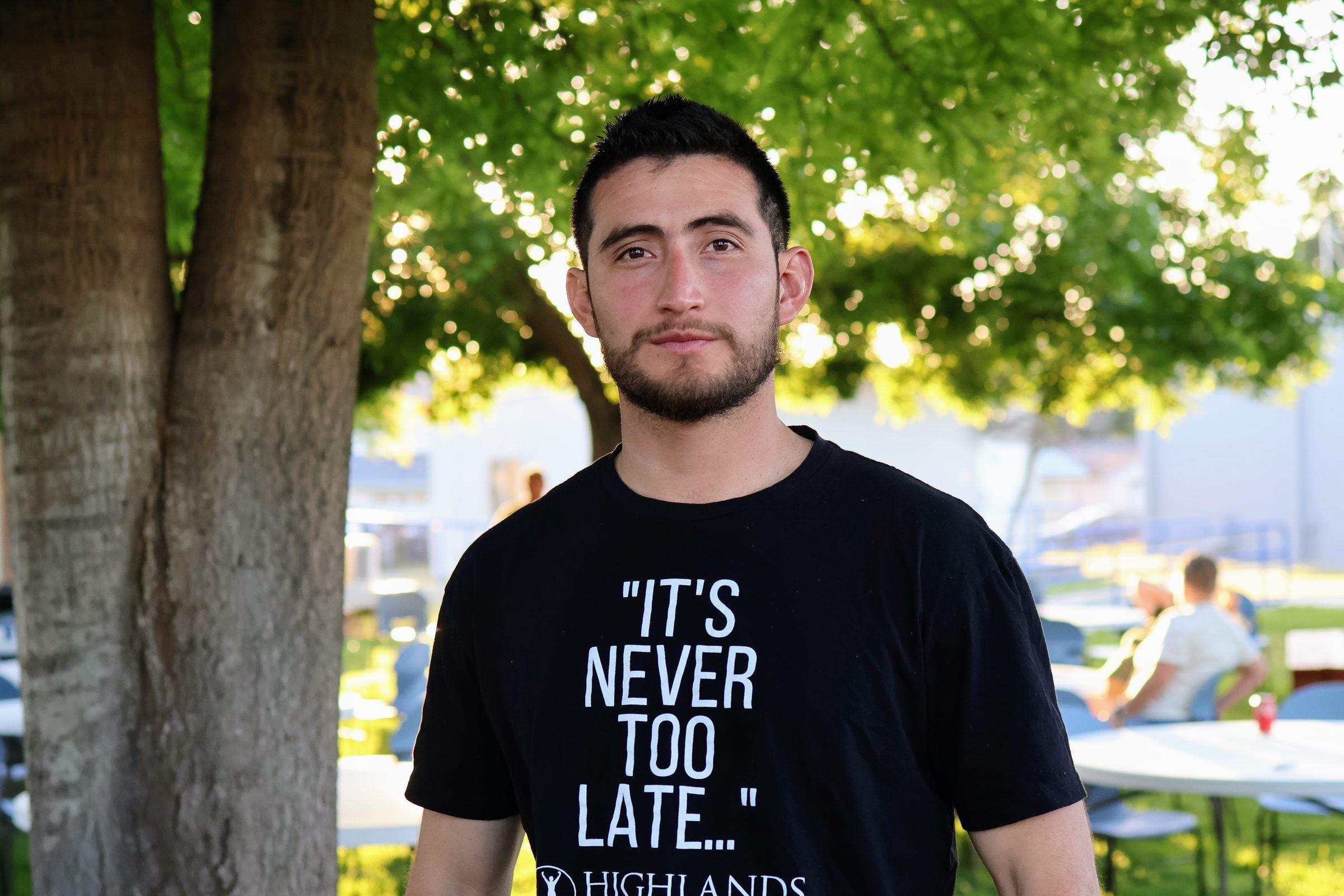 A community member wearing a Highlands Community Charter School shirt standing outdoors under a tree.