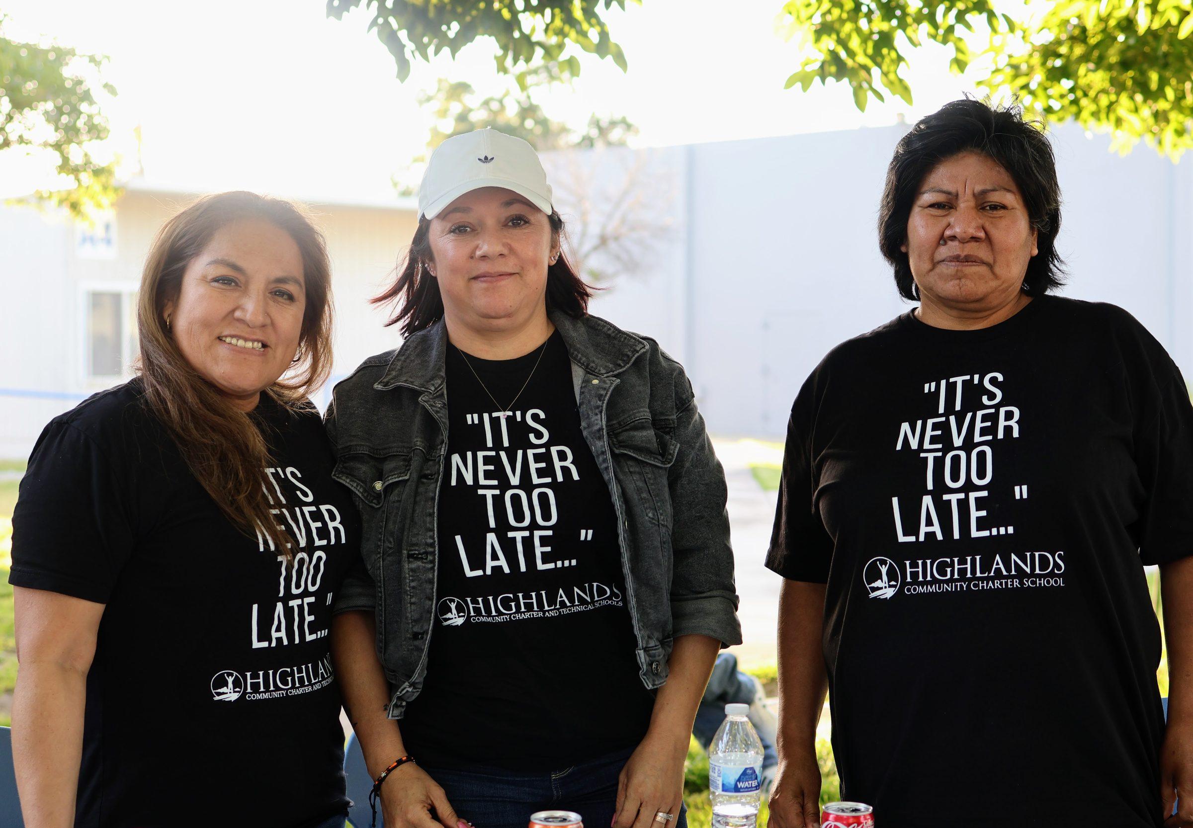 Three community members in matching Highlands shirts smiling together outdoors.